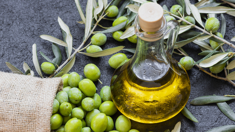 bottle of olive oil with green olives around it