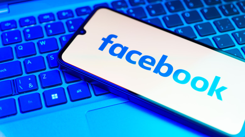 Smartphone sitting on laptop keyboard, with Facebook logo on it