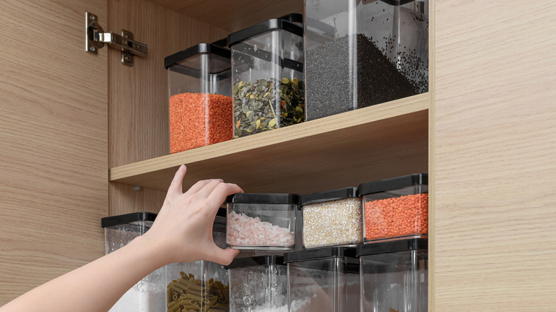 A hand reaching for a container of food in a cupboard
