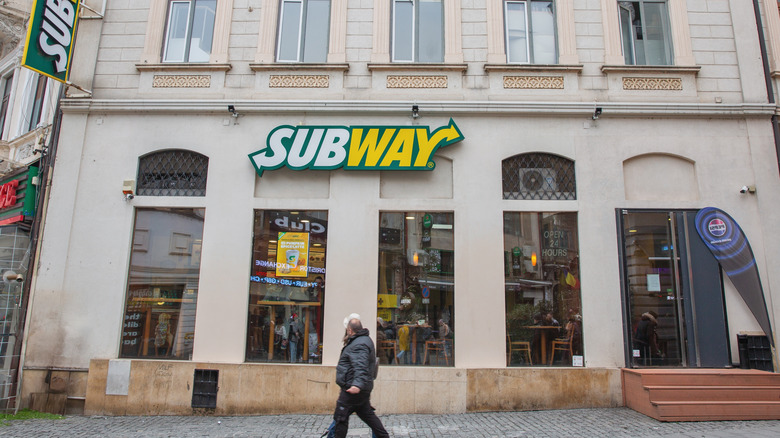 A pair of people walk past a Subway restaurant