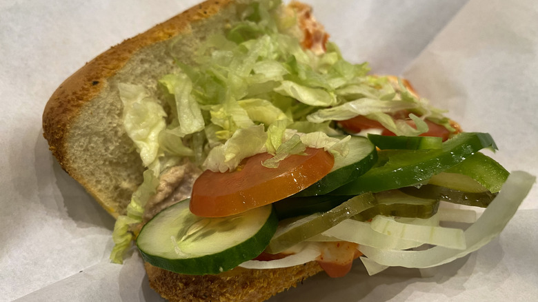 An open Subway sandwich with lettuce, tomato, cucumber, onion, and pickles.