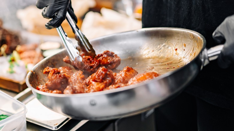 person cooking chicken wings in pan