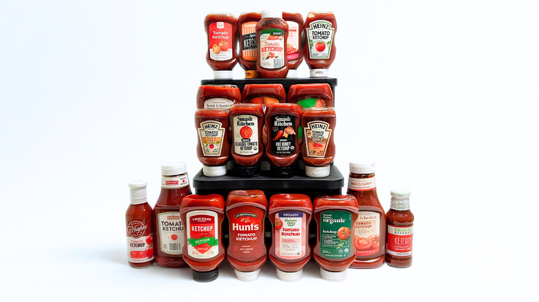 Many bottles of ketchups from different brands arranged together in several vertical rows