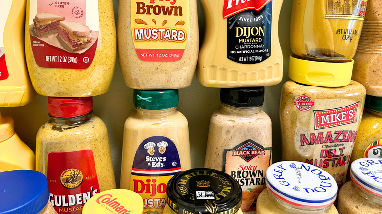 Close up of many bottles of different types of mustard from various brands arranged together
