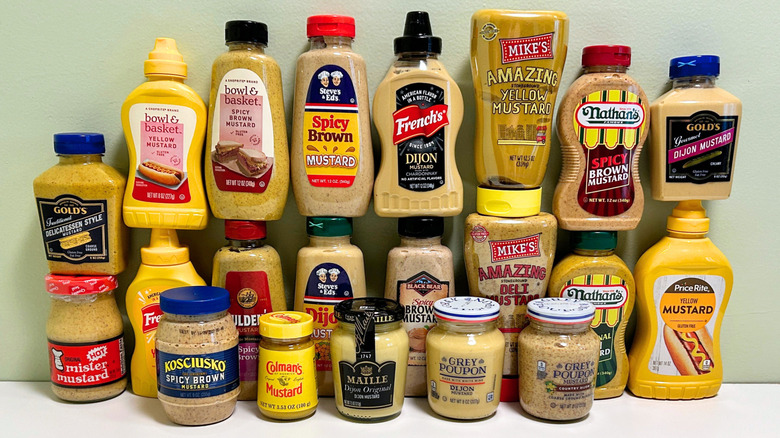 Many bottles of different types of mustards from different brands arranged together