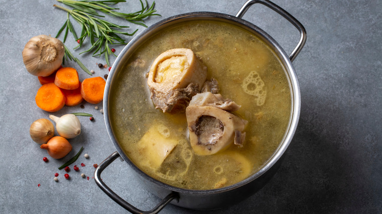 A pot of bone broth has vegetables next to it.