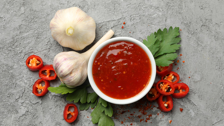 A bowl of chili garlic sauce is surrounded by its raw ingredients.