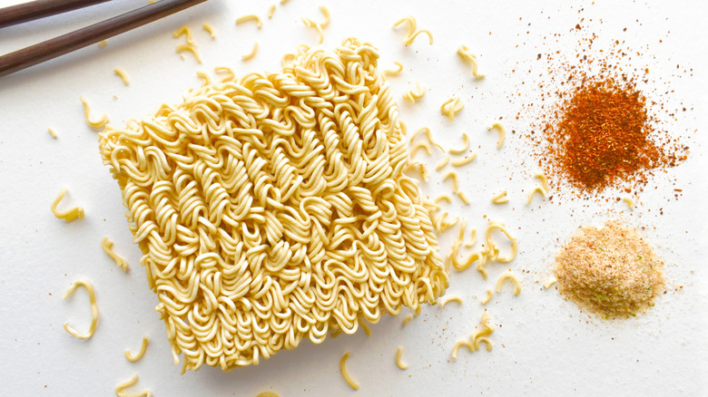 Uncooked instant noodles sit next to piles of dry seasoning.
