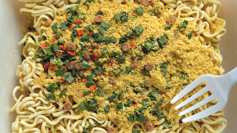 Uncooked ramen noodles have seasoning packet powder sprinkled on top.