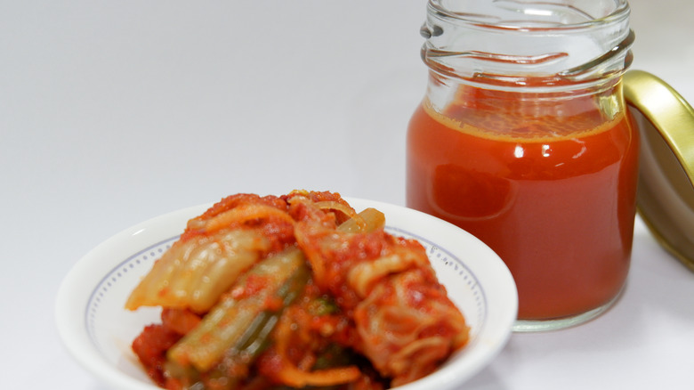 A bowl of kimchi is displayed with kimchi juice in a jar in the background.