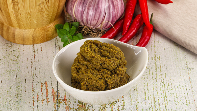 A white bowl of yellow Thai curry paste sits in front of some other ingredients.