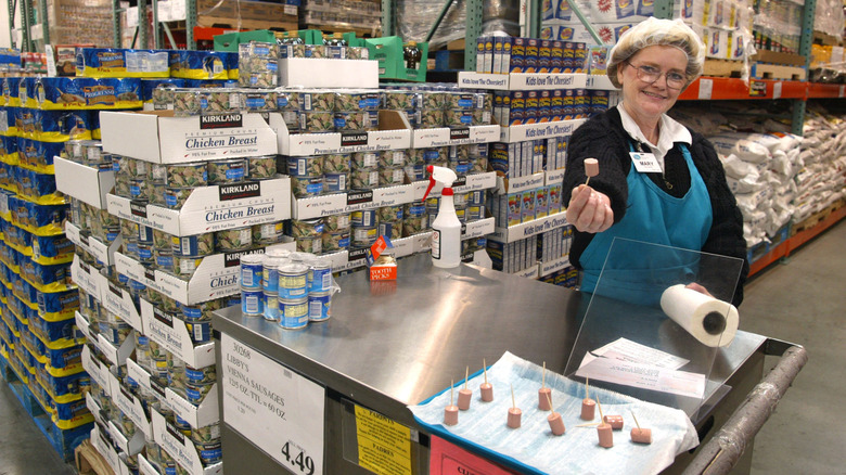 Female sample representative wearing a hairnet, holding up a sample of Libby's Vienna Sausage on a cocktail stick and smiling