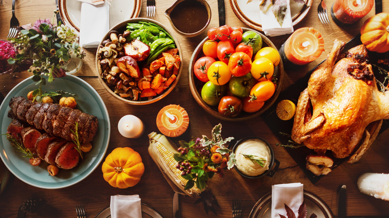 Top down view of a Thanksgiving spread with turkey, beef, and several vegetables and decorative gourds