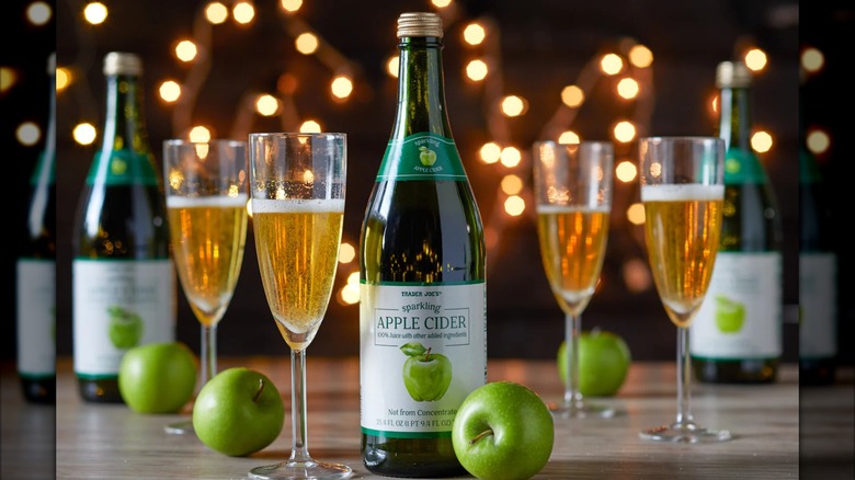 Bottles of Trader Joe's sparkling apple cider with champagne flutes of cider and green apples