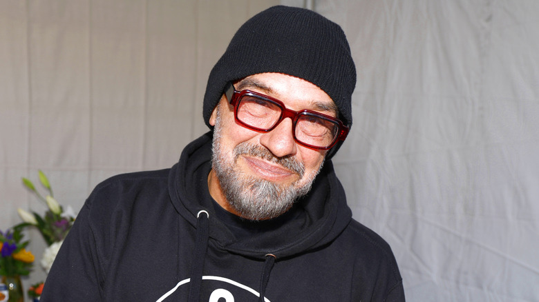 Michael Symon smiling, wearing a beanie hat and red framed glasses