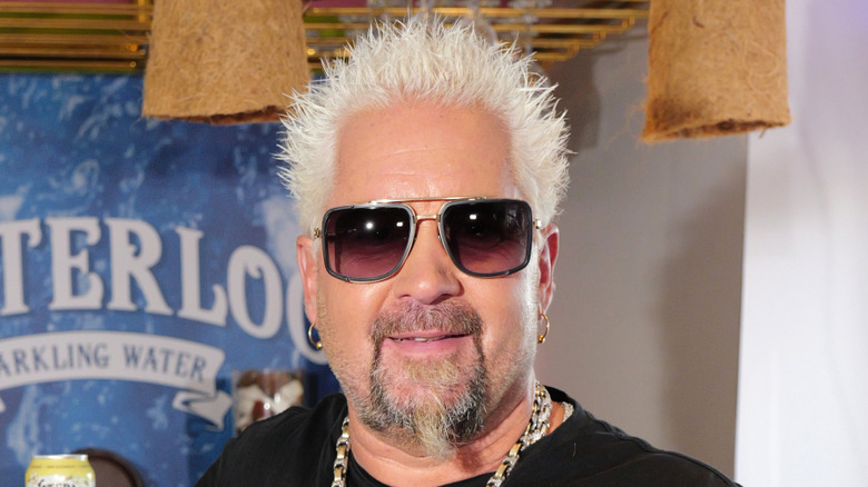 Guy Fieri with his trademark goatee, sunglasses, and bleached spiky hair.