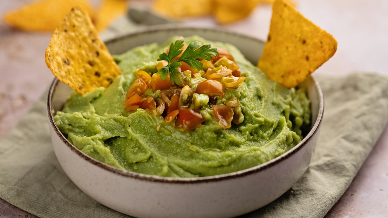 Bowl of guacamole, with tortilla chips in it and salsa ganish