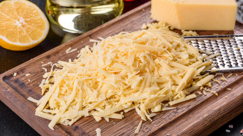 Shredded cheddar on a wooden board with a metal grater
