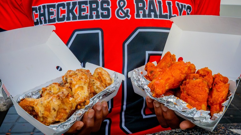 Close-up of man wearing a Checkers & Rally's jersey and holding two flavors of wings