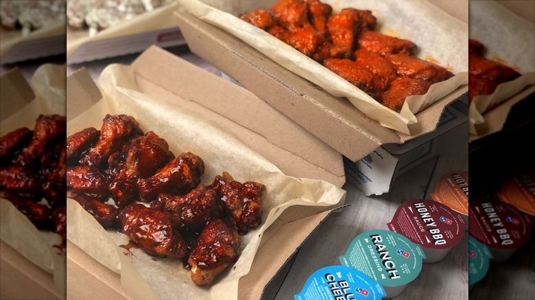 Two flavors of saucy Domino's wings in to-go boxes with various dips on the side