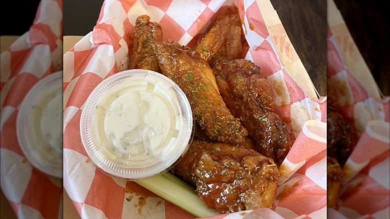 Hangry Joe's Hot Chicken wings in a to-go container with red and white checkered paper and dipping sauce