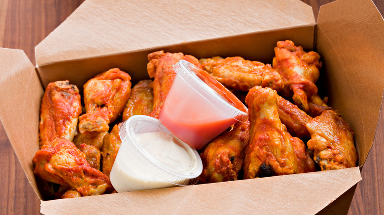 Brown fast-food, to-go box full of hot wings and two sauce containers