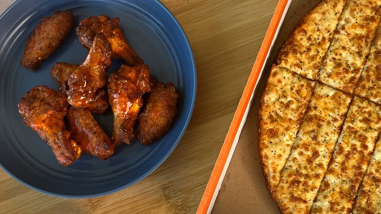 Little Caesars' saucy wings on a blue plate next to box of cheesy breadsticks