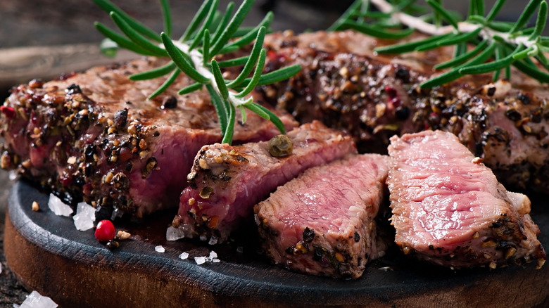 Close-up of sliced medium-rare steak with coarse salt, peppercorns, and sprigs of herbs
