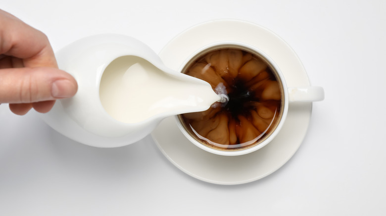 pouring creamer into coffee cup 