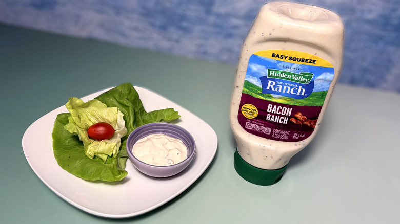 A bottle of bacon ranch next to a plate with salad and a bowl of dressing