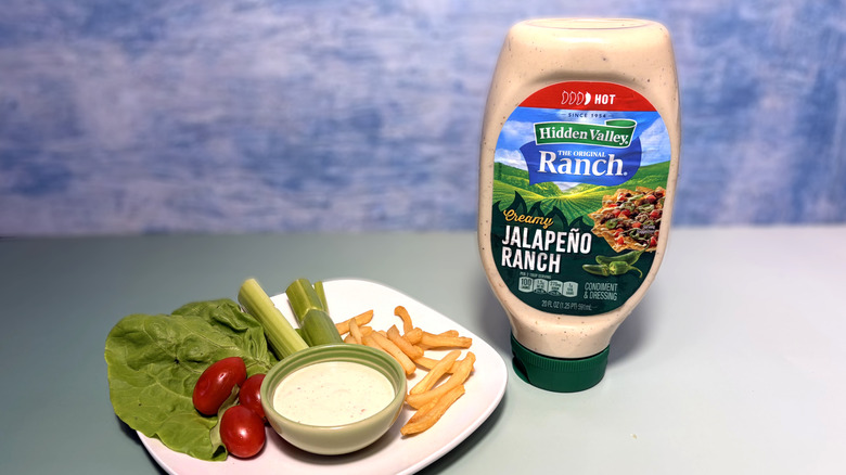 A bottle of jalapeño ranch next to a plate with salad, fries, and a bowl of dressing