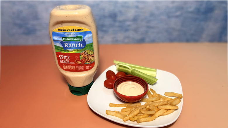 A bottle of spicy ranch next to a plate with celery, tomatoes, fries, and a bowl of dressing