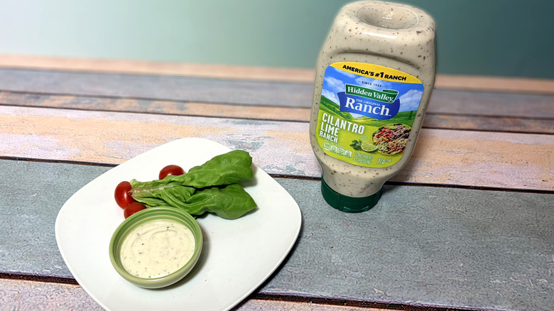 Bottle of cilantro lime ranch next to plate with salad and bowl of dressing