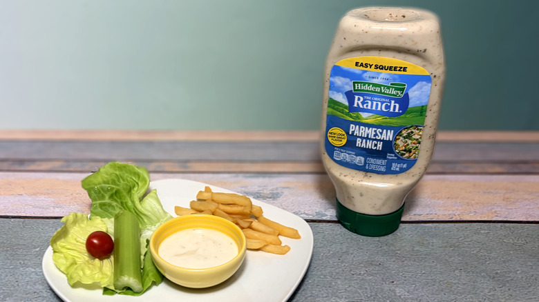 A bottle of parmesan ranch next to a plate with salad, fries, and a bowl of dressing