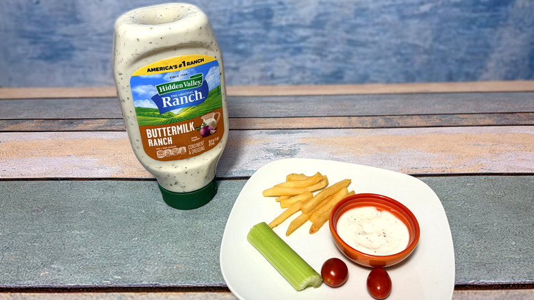 A bottle of buttermilk ranch next to a plate with celery, tomatoes, fries, and a bowl of dressing