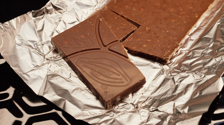 A bar of milk chocolate is broken into pieces on a foil wrapper.