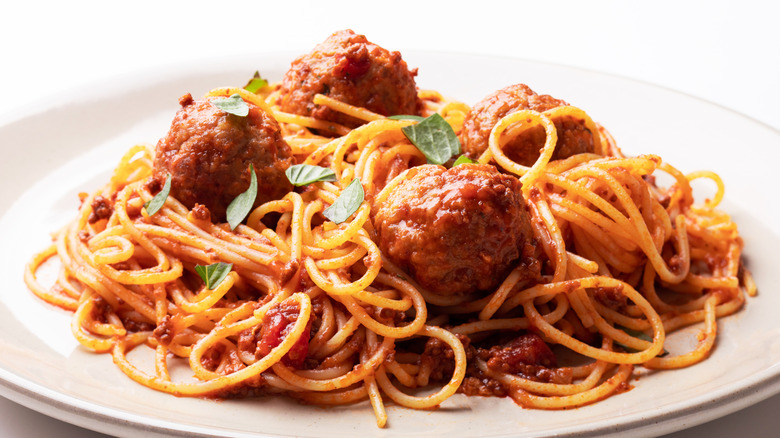 Spaghetti and meatballs with basil on a white plate
