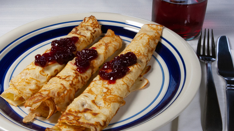 Three rolled up Swedish pancakes topped with jam on a diner plate with cutlery