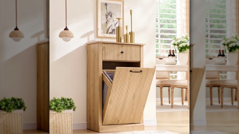 Tilt-out trash can against wall with decor