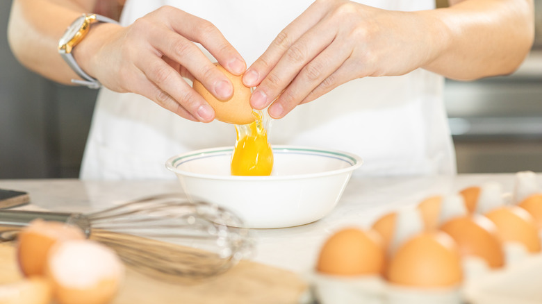 person cracking eggs into bowl