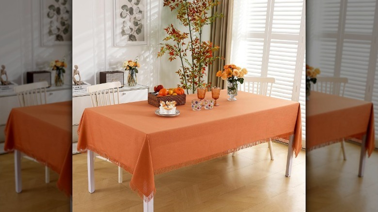 Orange fringed tablecloth on table in a dining room with flowers and glassware