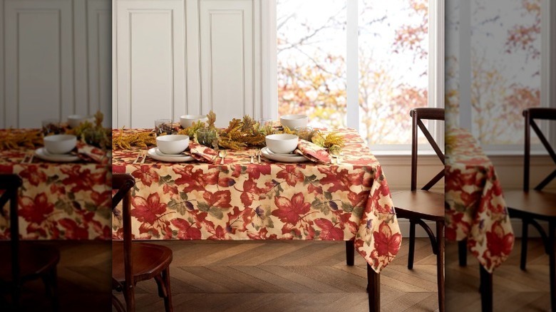 Orange autumnal leaf tablecloth on table with fall decor and meal settings