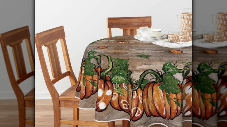Rustic pumpkin tablecloth on round table with chairs and dinnerware