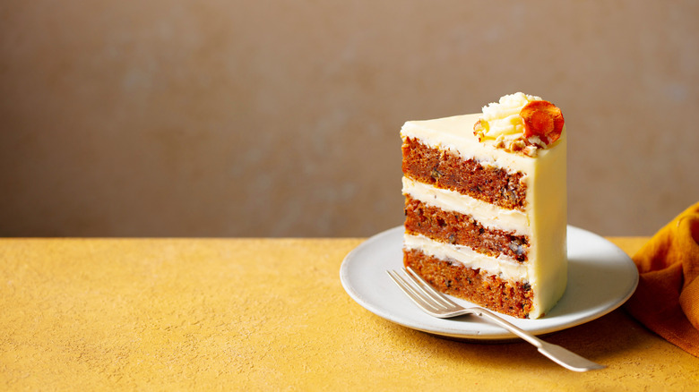 A beautiful slice of carrot cake on a yellow tabletop