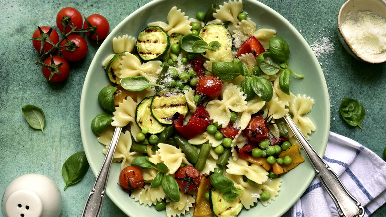 A pasta primavera with bright vegetables and tomatoes on the side