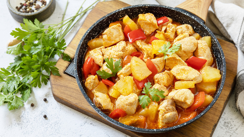 A pan with pineapple chicken garnished with sprigs of parsley