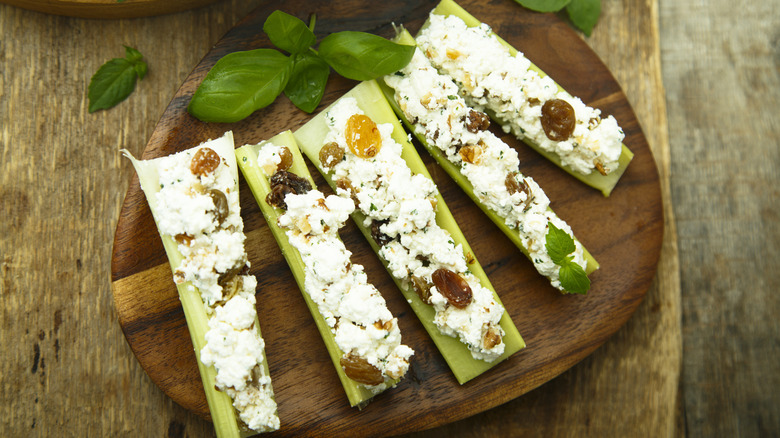 Celery logs stuffed with cream cheese and raisins on a wooden plate