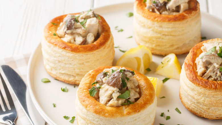 Four vol-au-vents with chicken fillings arranged on a plate with lemon wedges