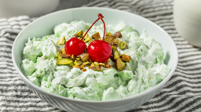 A bowl of Watergate salad garnished with maraschino cherries and pistachio pieces