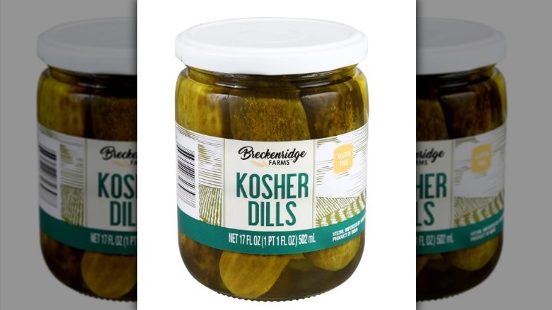 Kosher dills jar with pickles inside and a white lid on white background